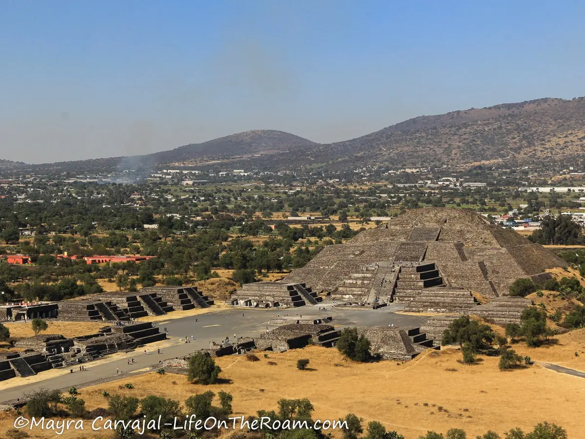 A large pyramid at the end of a wide walkway with mountains in the background