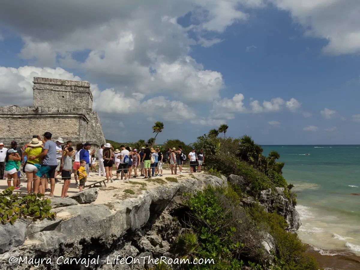 People walking along a cliff with views of the sea and an ancient temple