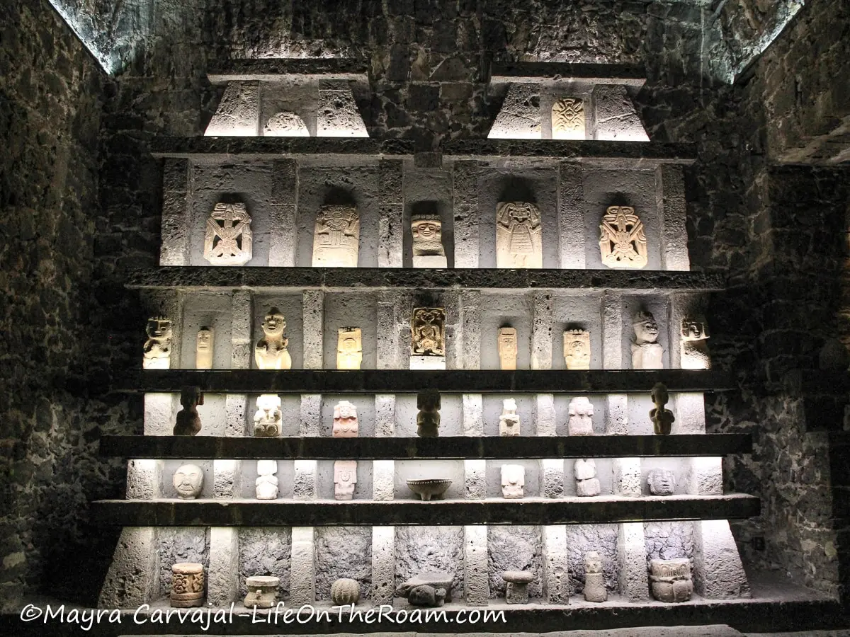 Ancient artifacts arranged in shelves recessed in stone with altar-like shape
