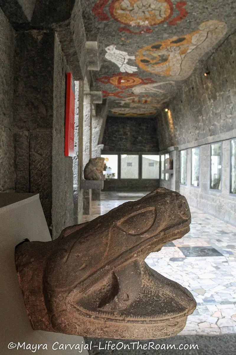 A head serpent in stone in a hallway with stone mosaics in the ceiling