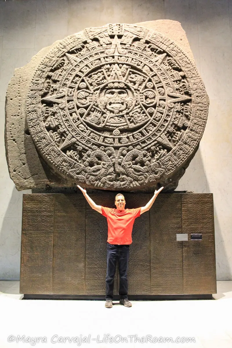 Man standing in front of an ancient large stone sculpture shaped as a disc, with elaborate carvings