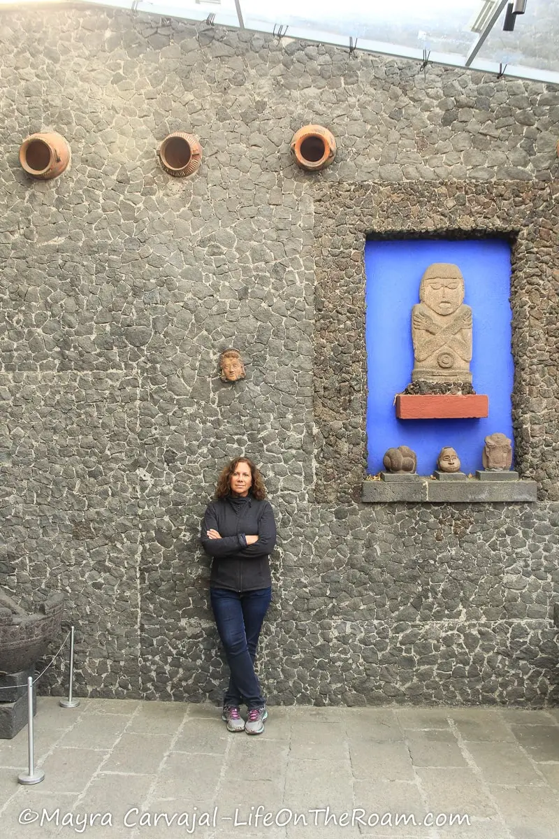 Mayra in a patio with stone walls and pre-Hispanic pottery