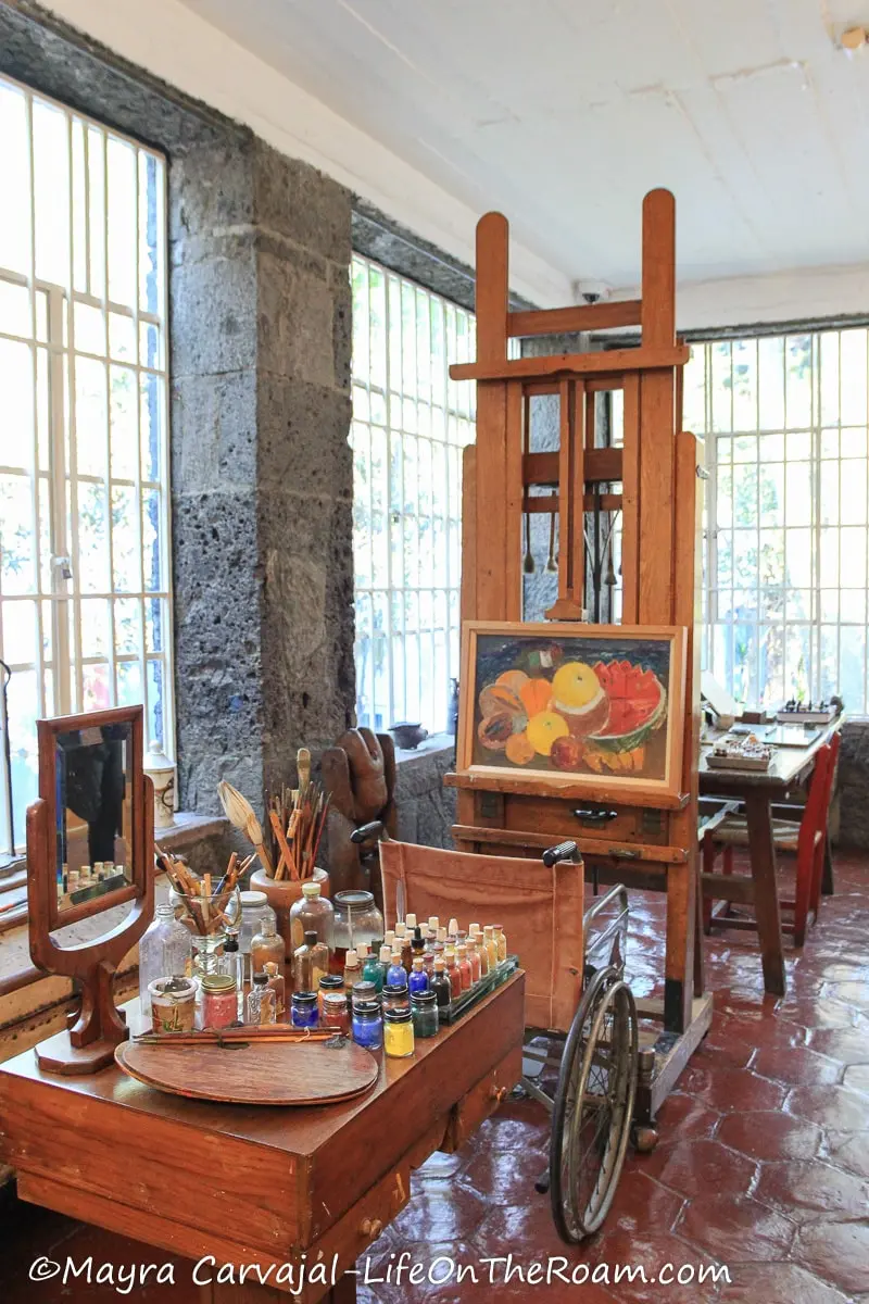 A sunlit room with a wheelchair, an easel, and art supplies