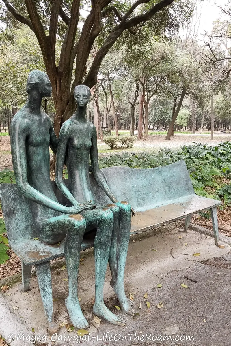 A metal bench with two human-like sculptures