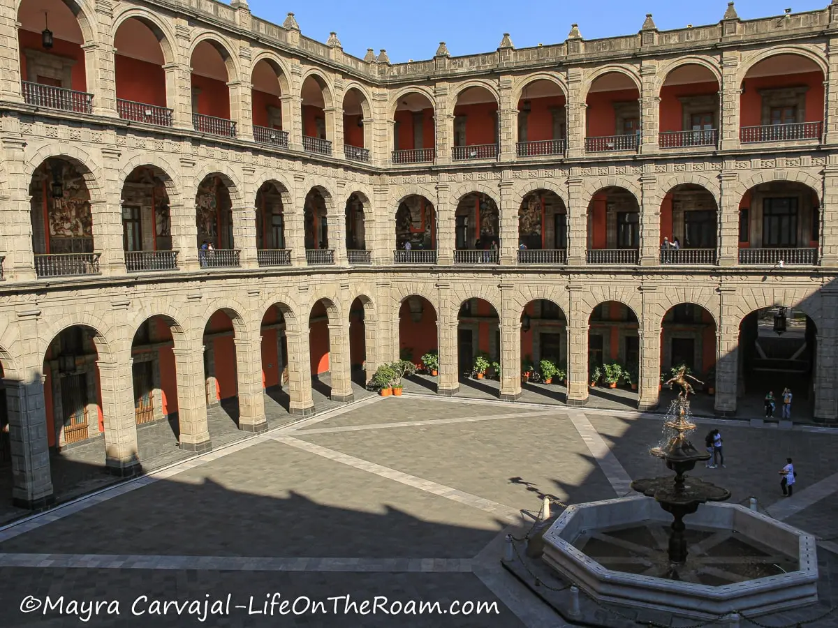 A patio in a palace with three stories of arches and a fountain in the centre