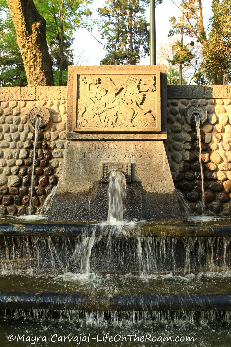 A carved stone in a fountain depicting life scenes