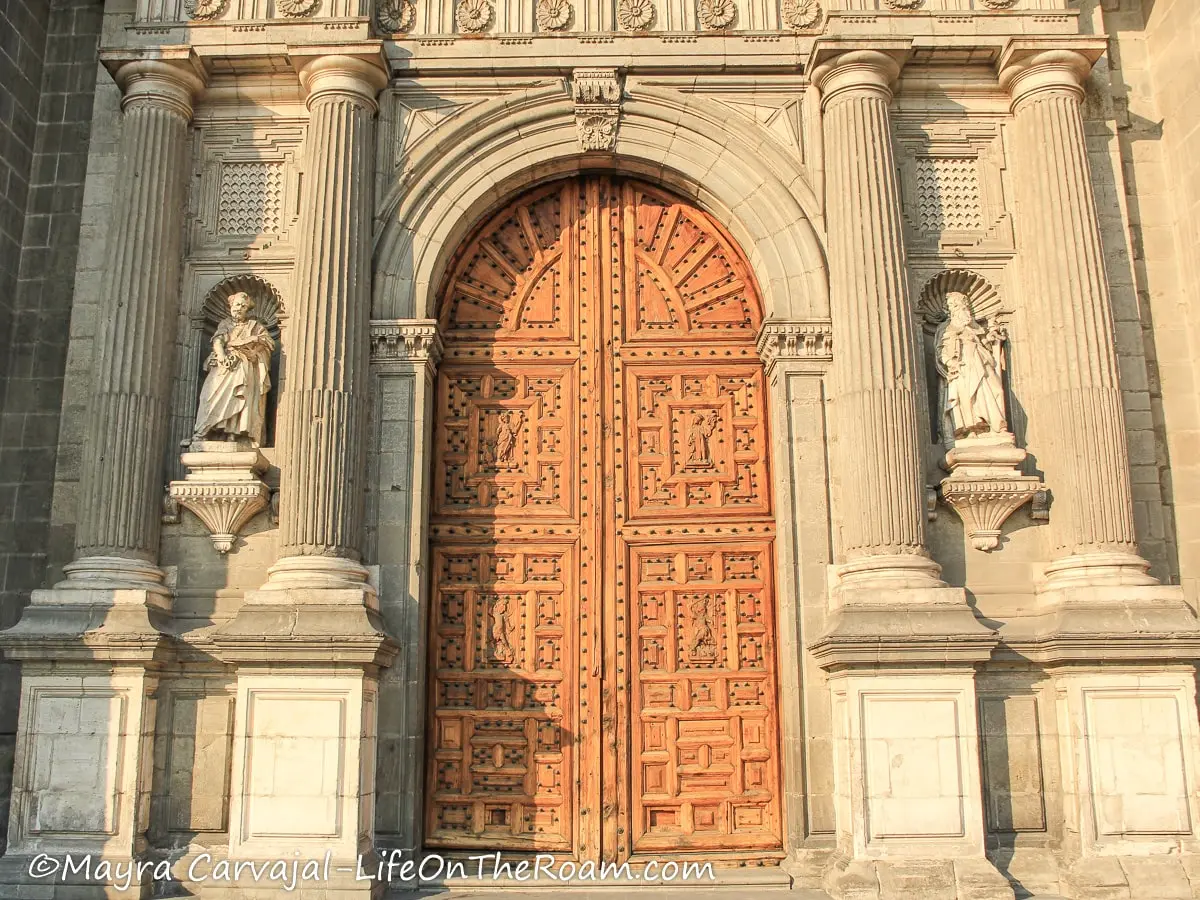 A tall and wide wood door flaked by columns and statues in a 16th century cathedral
