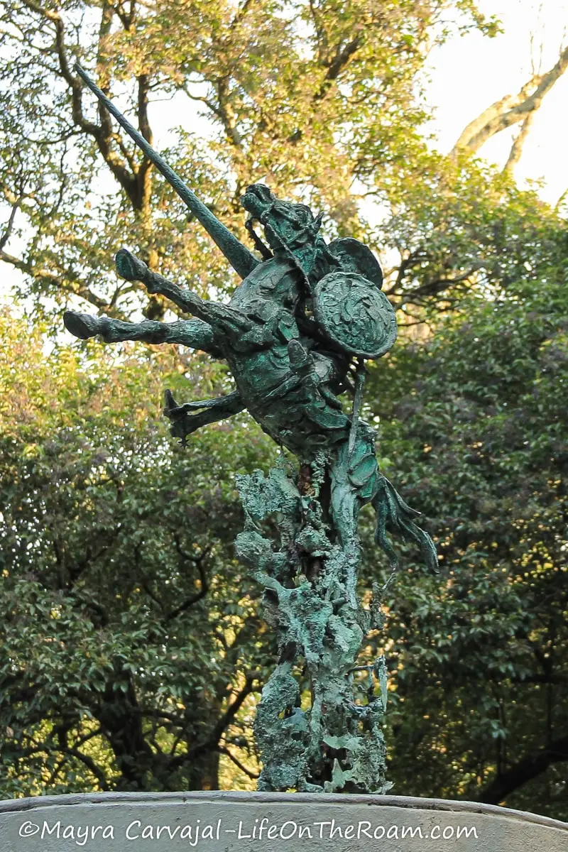 A metal sculpture of a man in a horse in a park with trees