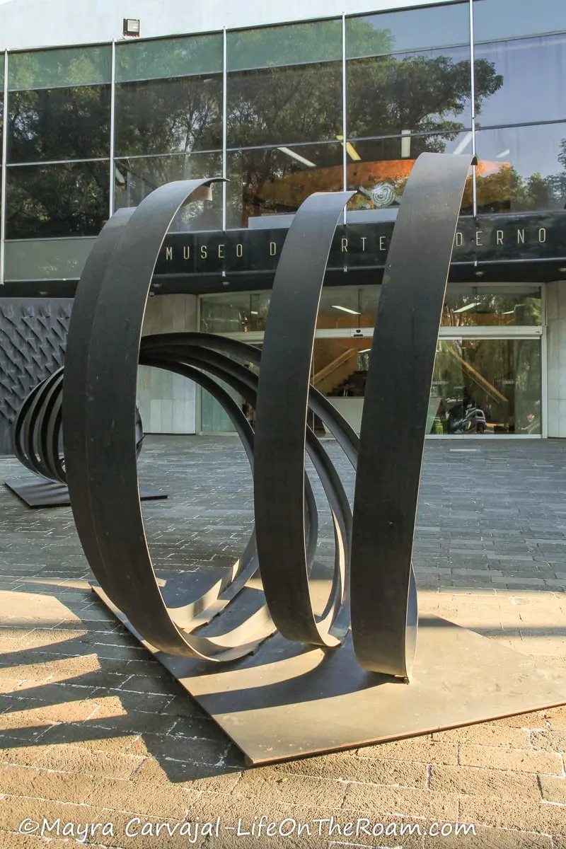 A modern sculpture in front of a glass-clad building with the name "Museo de Arte Moderno"