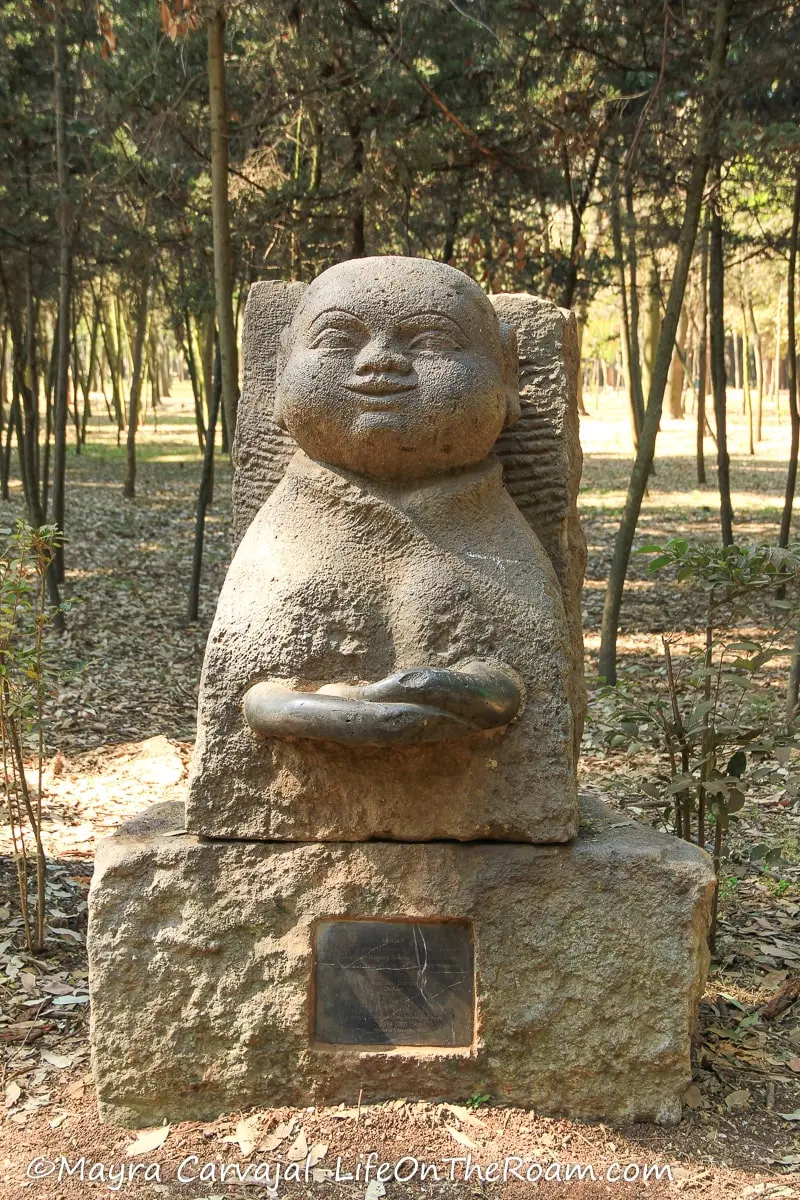A stone sculpture in a park, looking like a monk