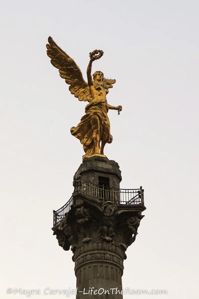 A golden statue of an angel-like figure holding a wreath at the top of a stone column