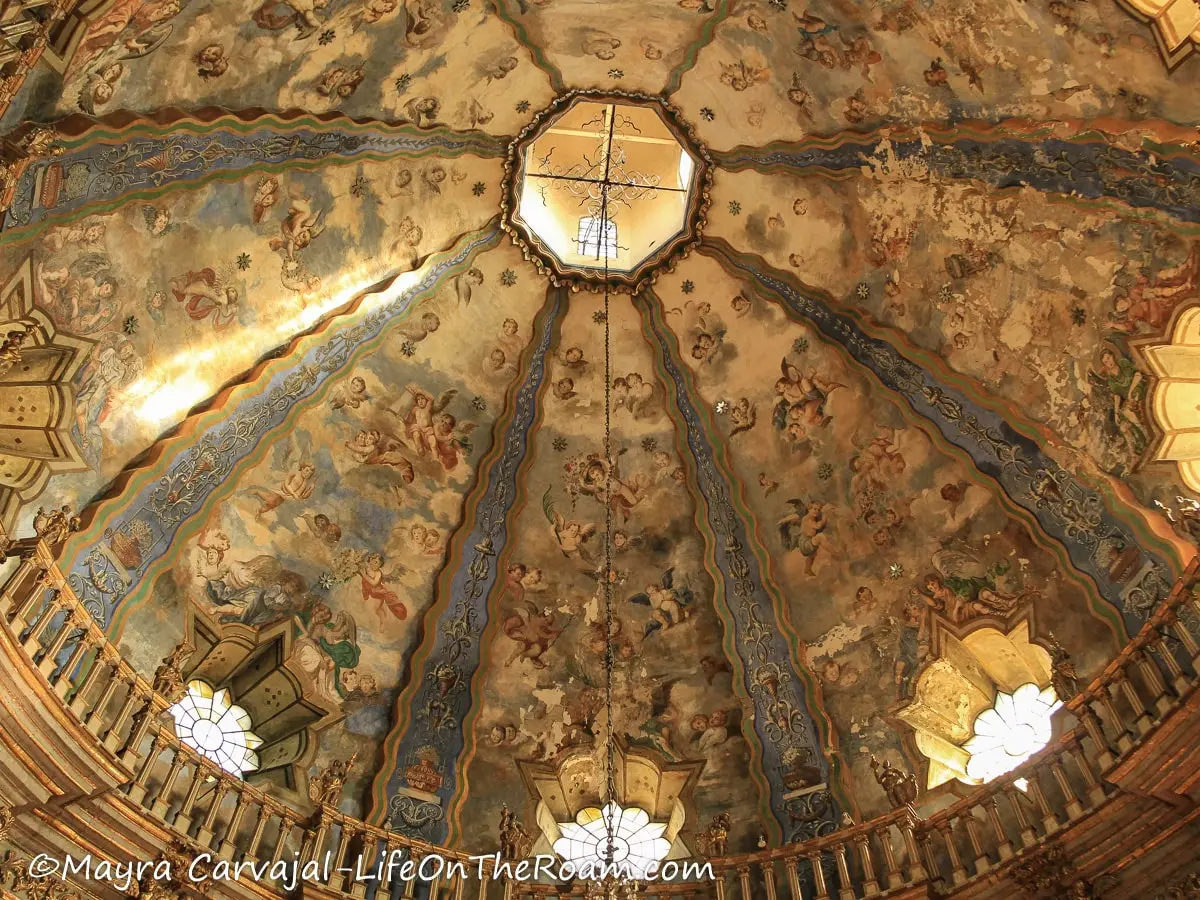 A richly decorated dome inside a chapel, with gold and blue details and depictions of angels