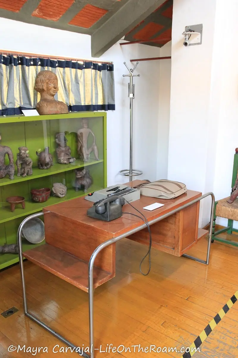 An old metal and wood office desk with a green shelving unit at the back with pottery