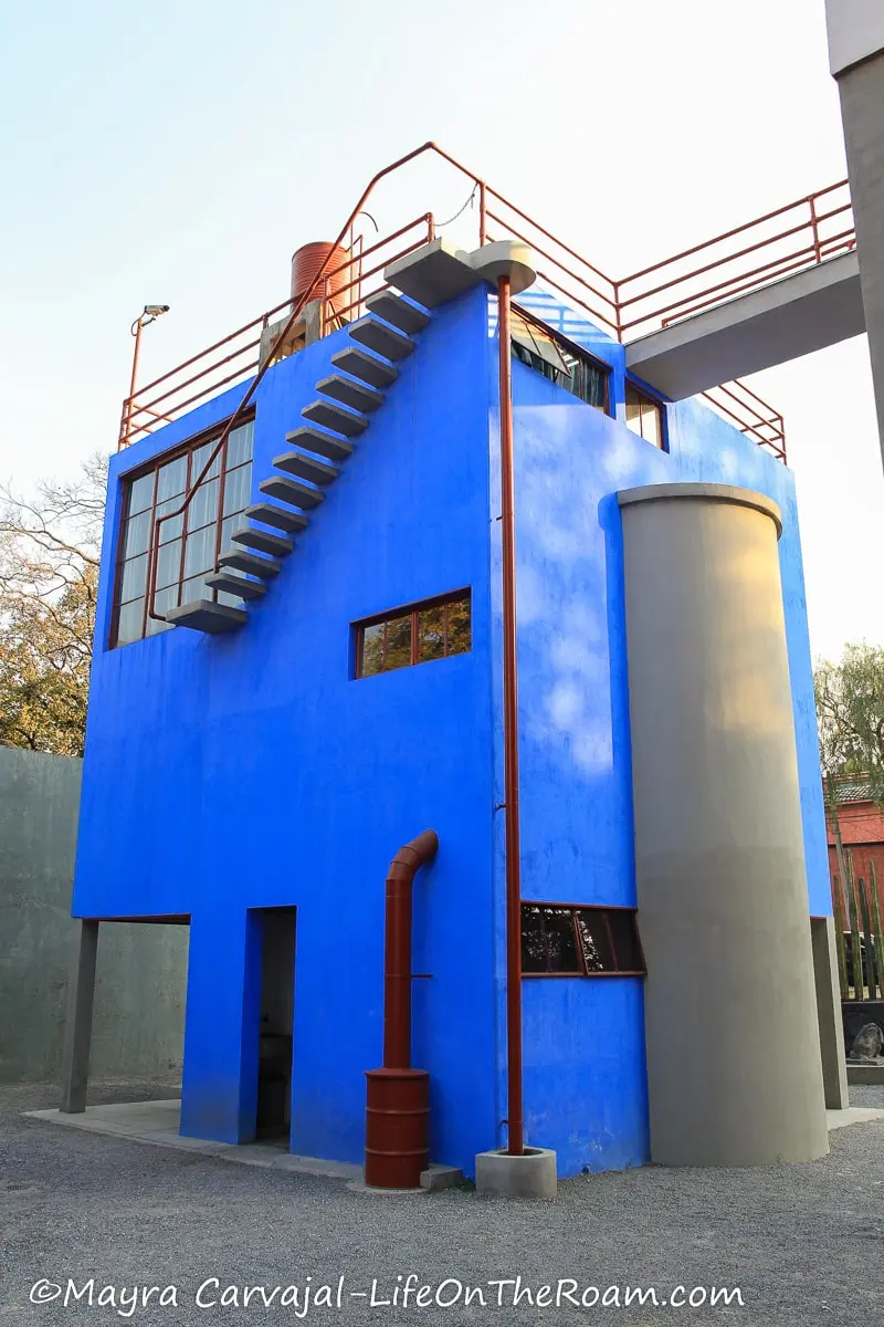 A rectangular 2-storey house painted in electric blue with red window mullions and rails