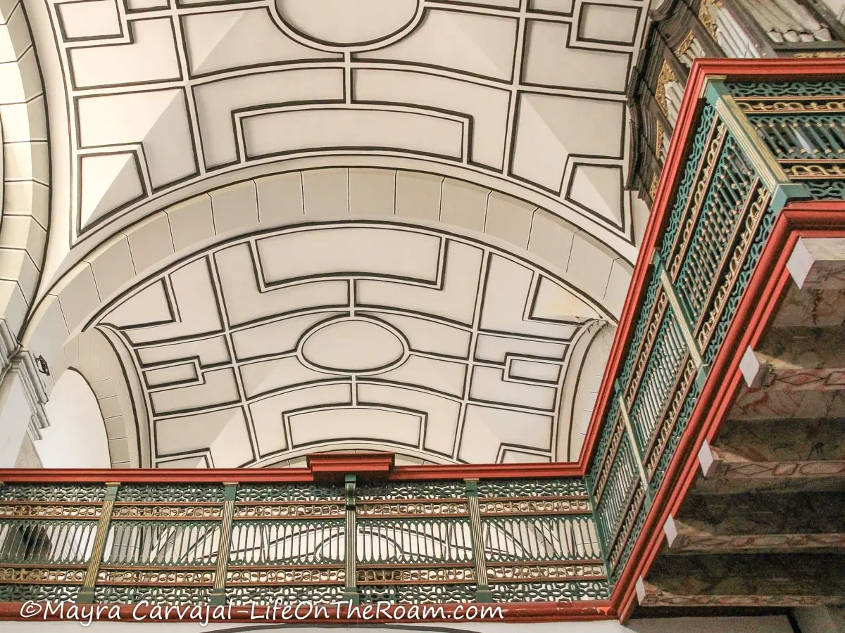 A detailed railing in an upper level inside a church with a decorated ceiling