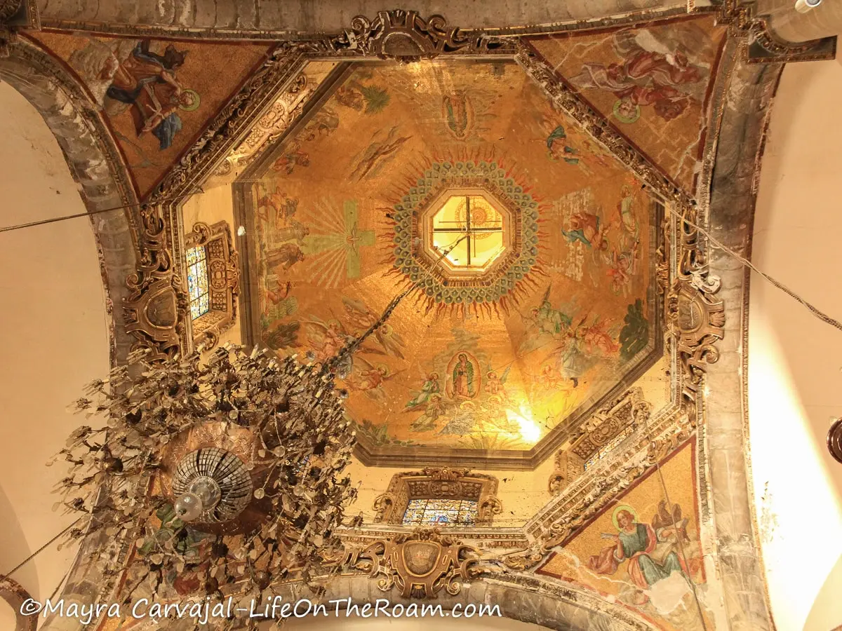A dome inside a church with gold tones and intricate details,, and a chandelier