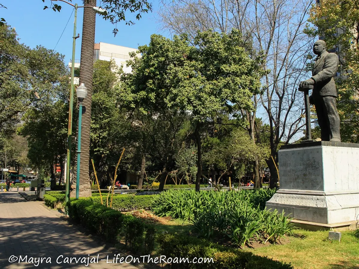 A statue of Martin Luther King Jr. in an urban park with tall trees