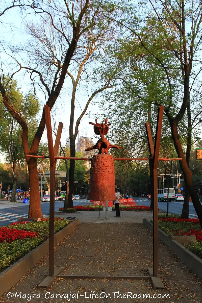 A sculpture resembling a bell in a wide landscaped avenue