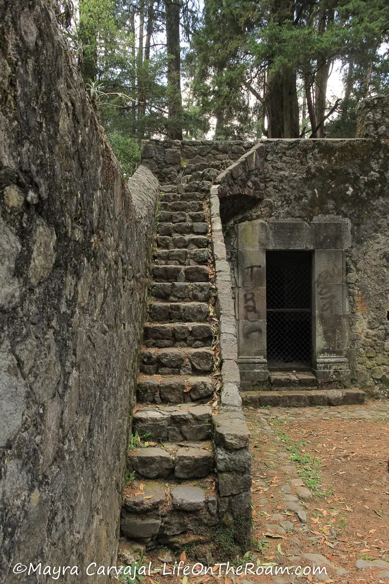 An old hermitage with stone walls with a stair along the left wall and a narrow entrance on the right