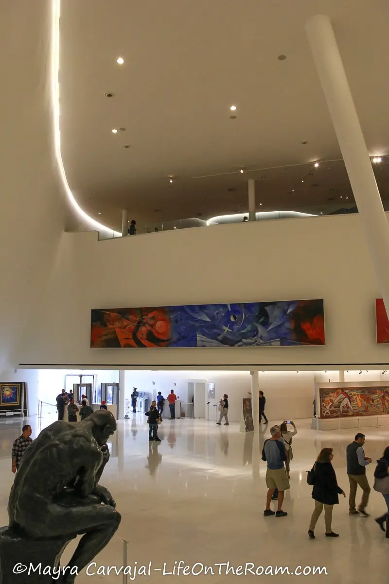 A sculpture at the lobby of a museum with large rectangular paintings