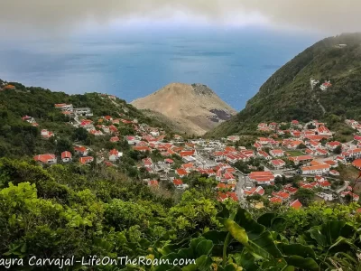 A view of a small village with red-roofed white houses in a valley with the ocean in the background on the island of Saba