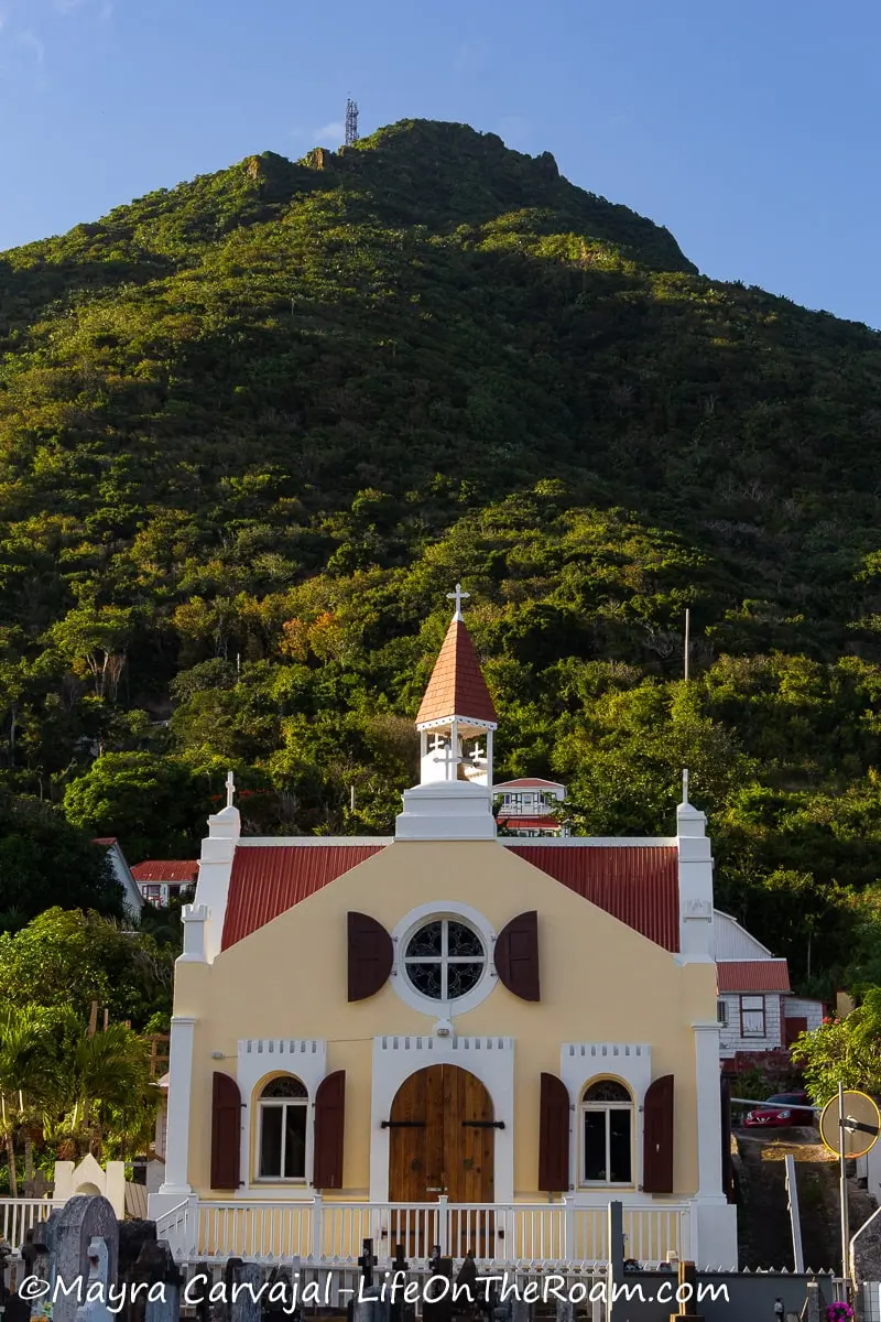 A church building in traditional style with red roof and trims with a mountain in the background