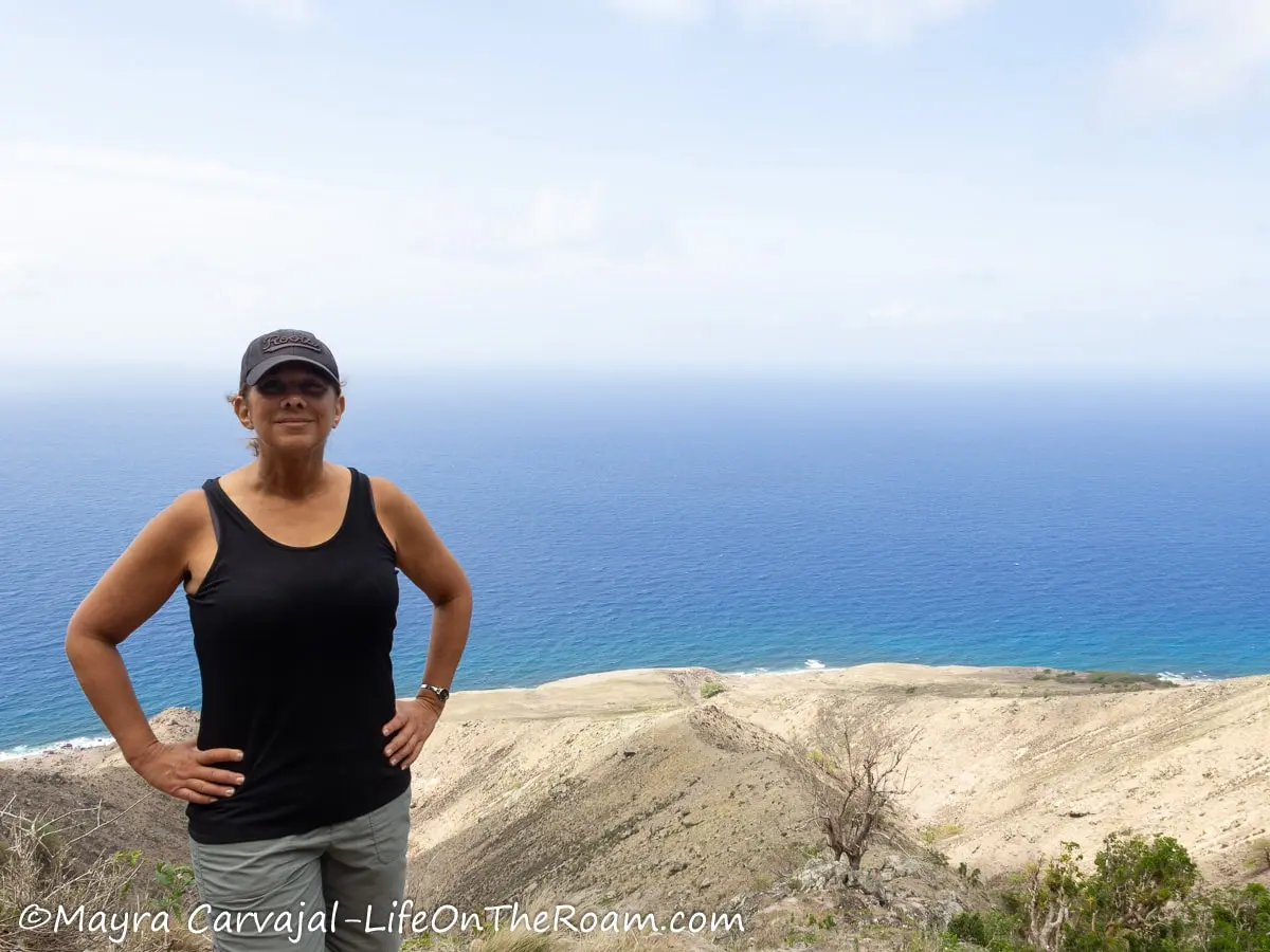 Mayra standing on a trail on Saba with views of a ridge leading to the ocean