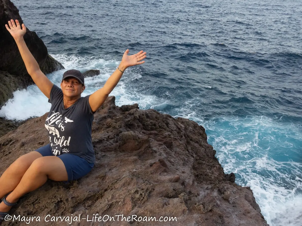 Mayra sitting on a lava rock formation next to the sea