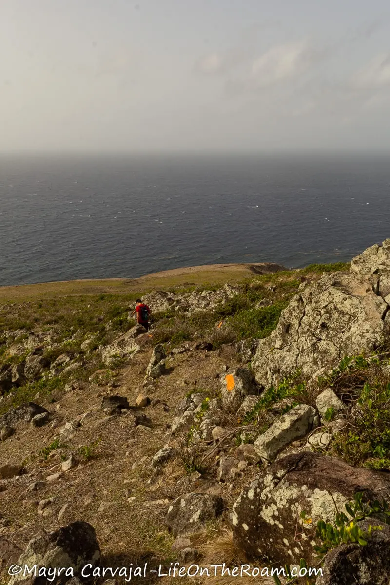 A man going downhill on a rocky and grassy ridge leading to the coast