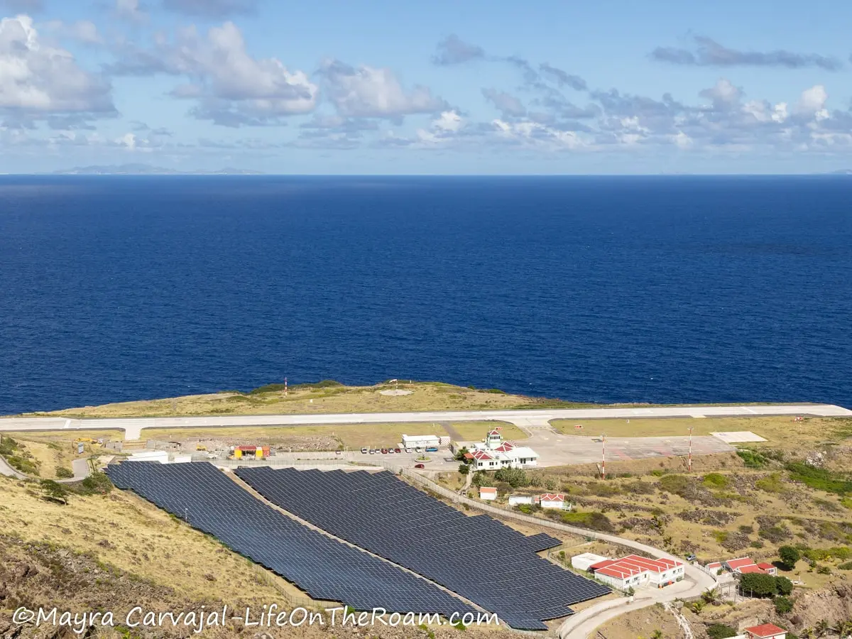 A short airplane runway with solar panels in the foreground and the sea in the background