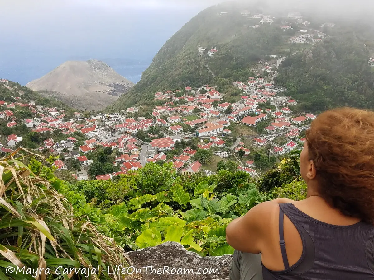 Mayra at a viewpoint looking into a small village in a mountain and the ocean in the distance