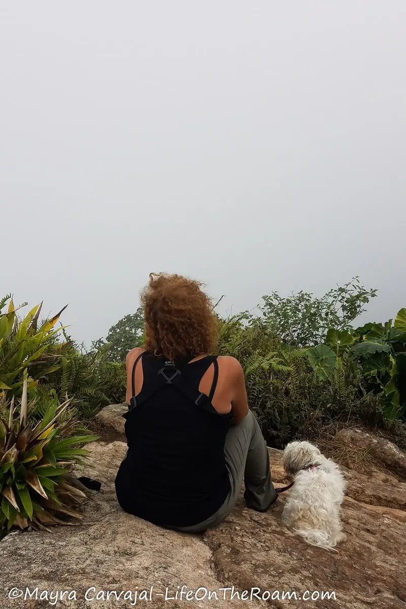 Mayra sitting on a rock next to a small dog while looking towards the cloud