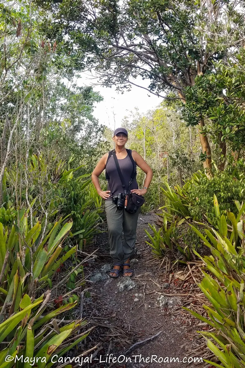Mayra standing in a rocky trail flanked by leafy trees and bromeliads