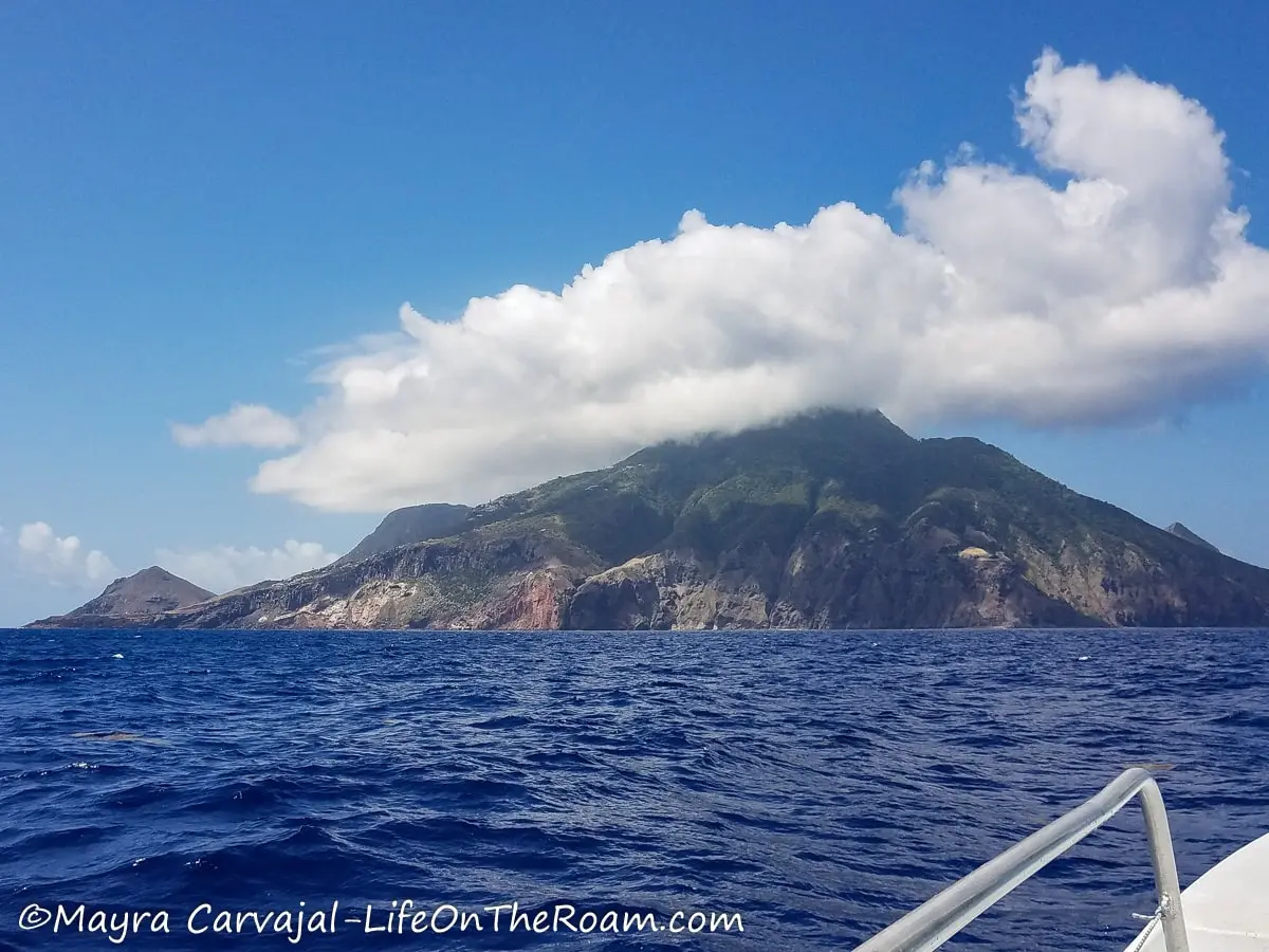The island of Saba, with a conical shape and a cloud on top seen from a boat