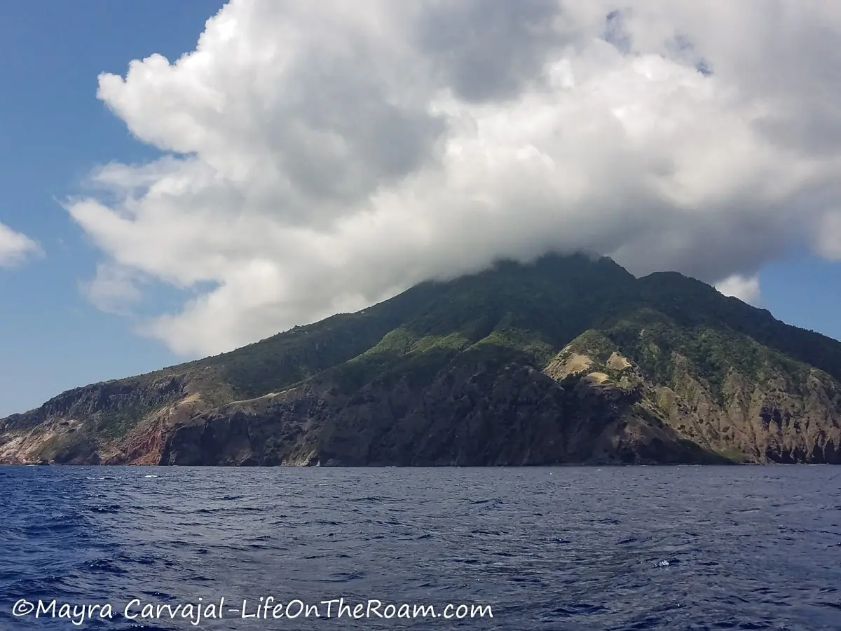 View from the water of the conical shape of the island of Saba, with a cloud on top