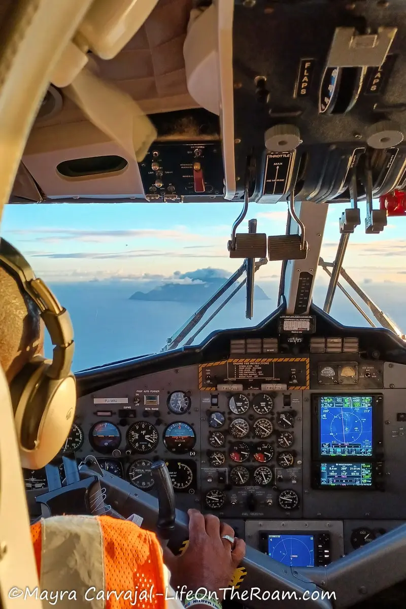 View of the island of Saba in the distance from the open cockpit of a small plane with plane instruments in the foreground