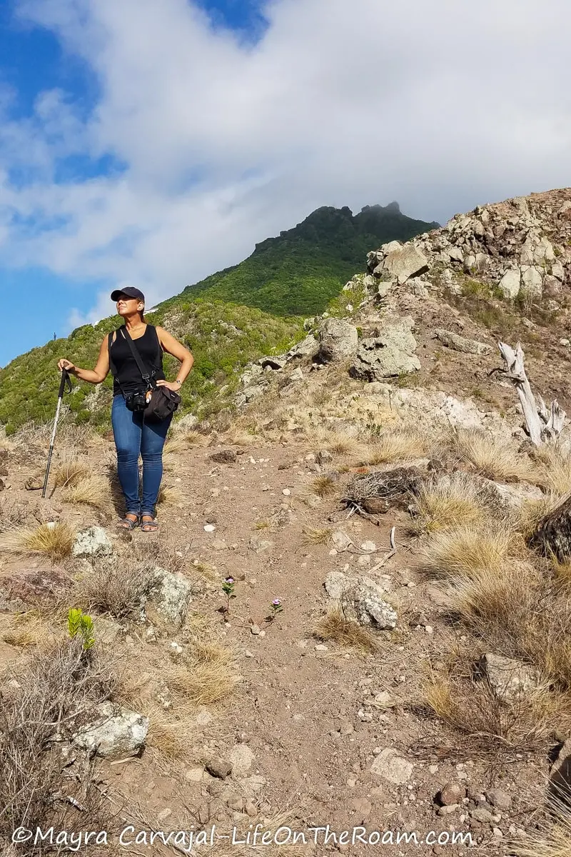Mayra standing on a rocky trail without trees with a view of a verdant mountain in the background