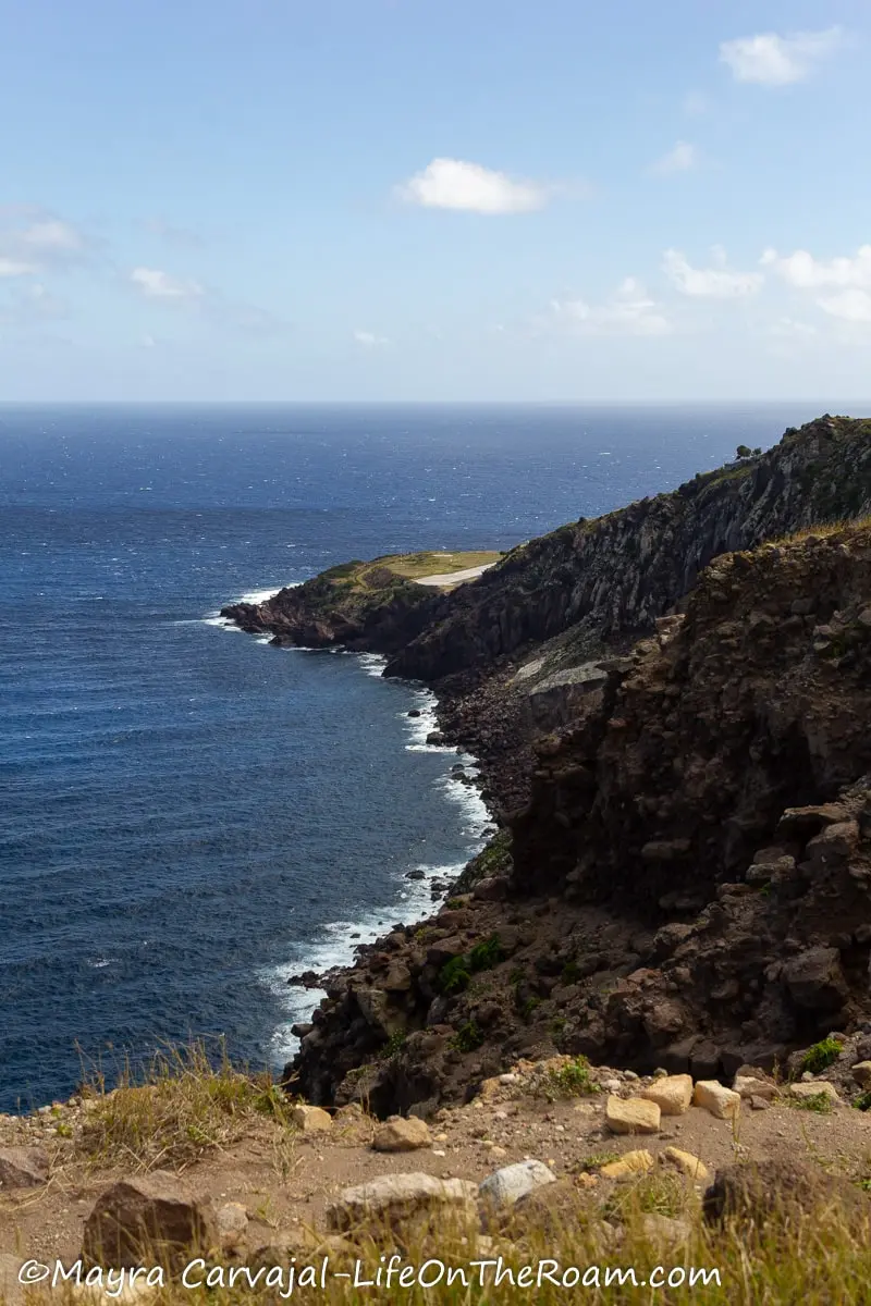 A rugged coastline with a hill descending into the ocean and a landing strip at the end
