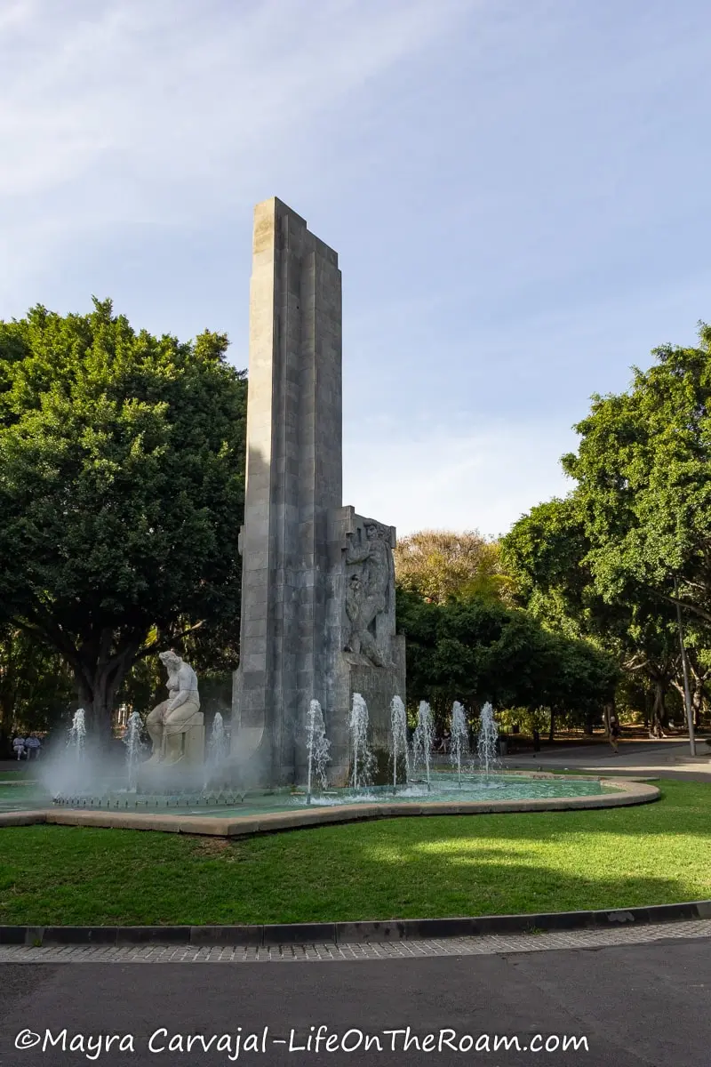 A monument with a big fountain in an urban park with mature trees