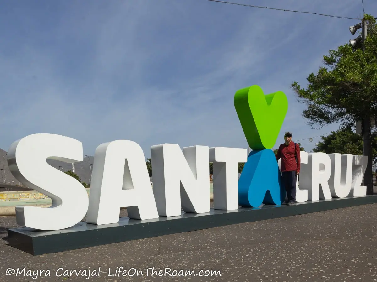 A man standing next to big white letters on a public square spelling SANTA CRUZ 
