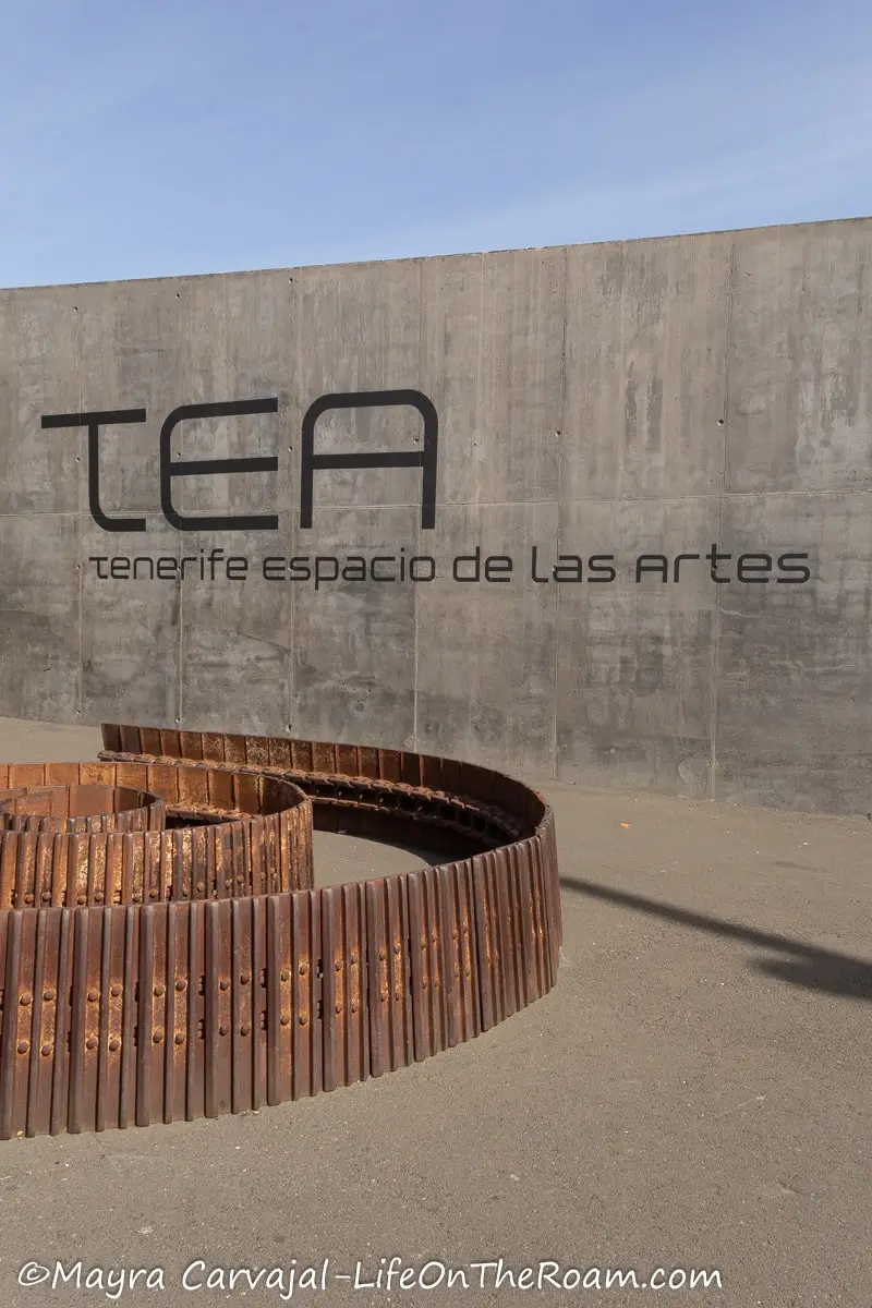 A sign on a curved wall with the letters TEA and a metal sculpture forming a curve