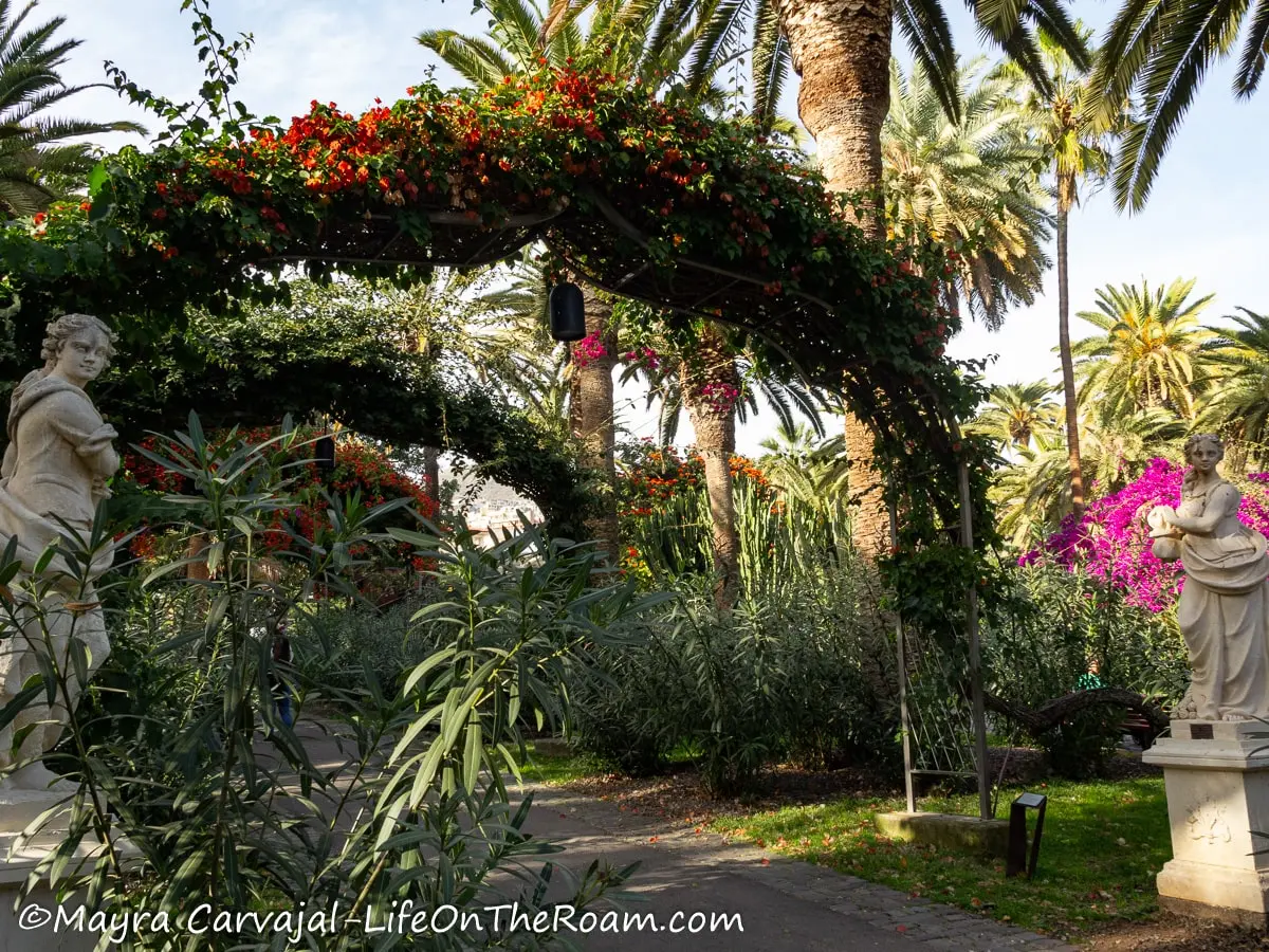 Two sculptures flanking the entrance of a series of arches covered in foliage and flowers 