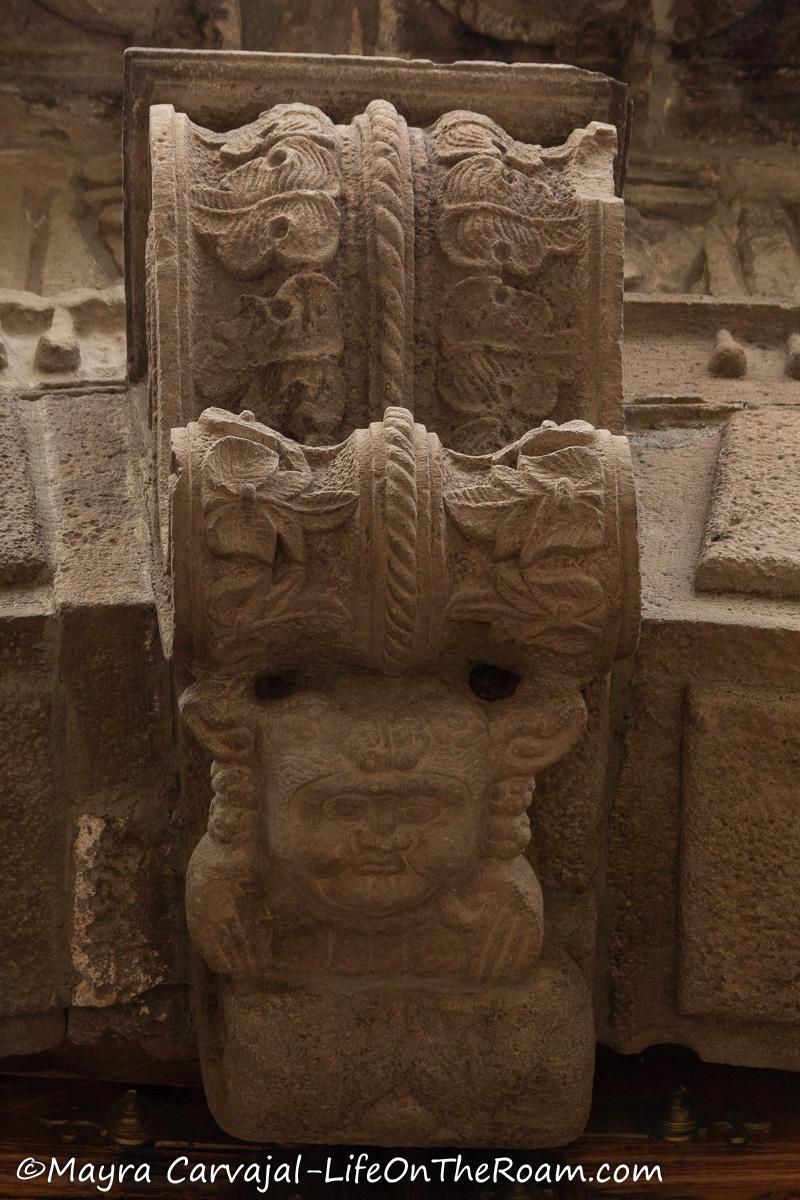 A stone sculpture with nature motifs and a human-like figure adorning the top of an arch