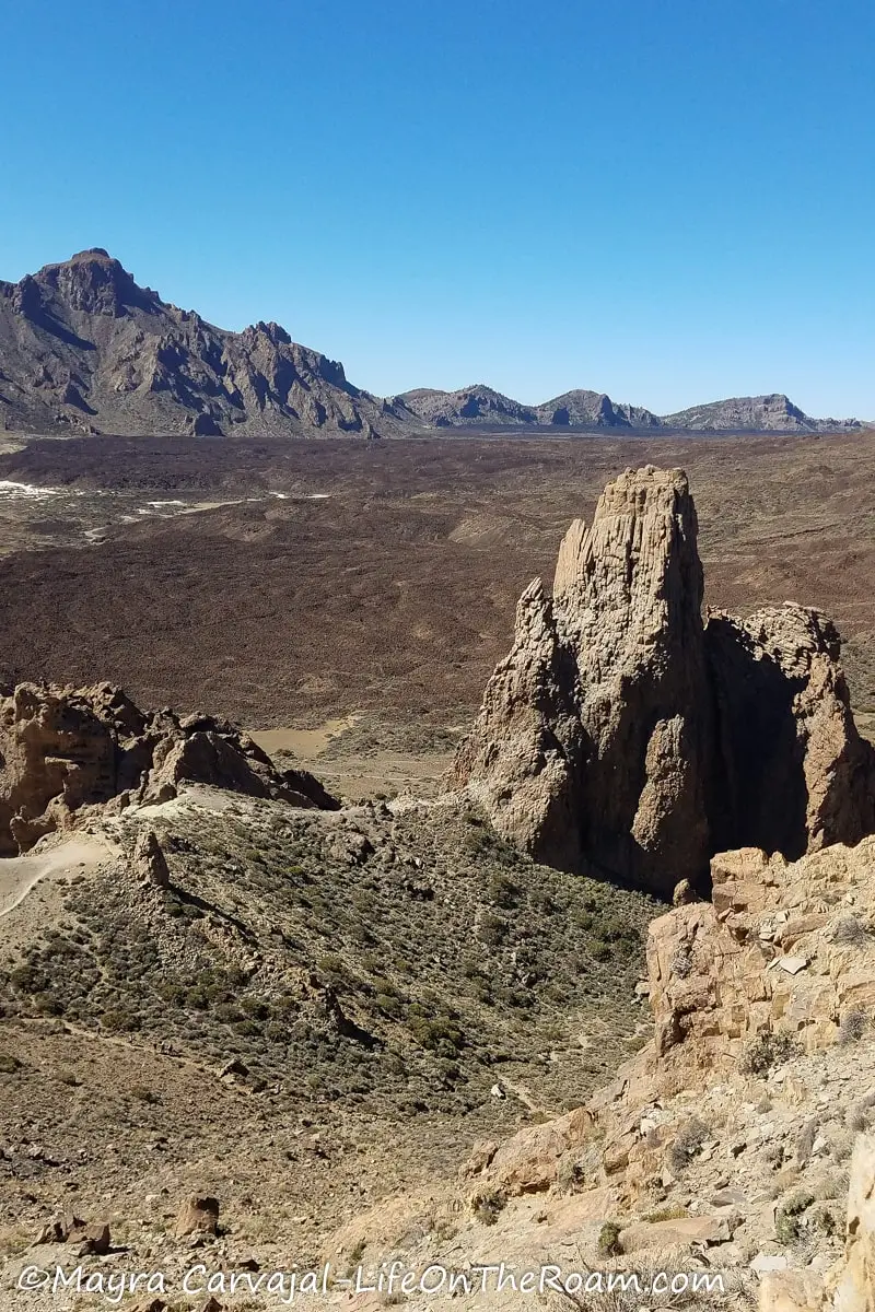 A rock formation resembling the shape of a church in a desert environment with mountains in the background