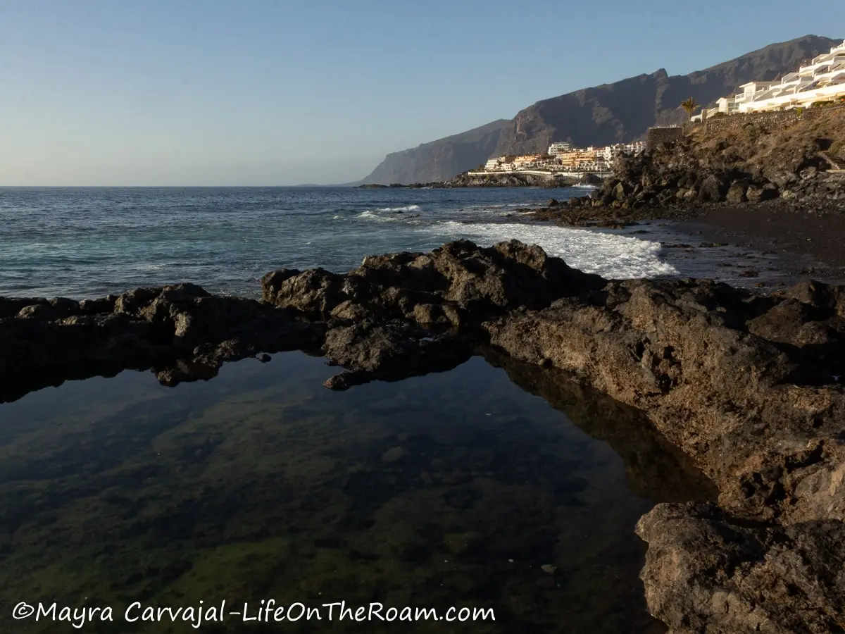 Rock formations along a sea shore forming ponds with the view of cliffs in the distance