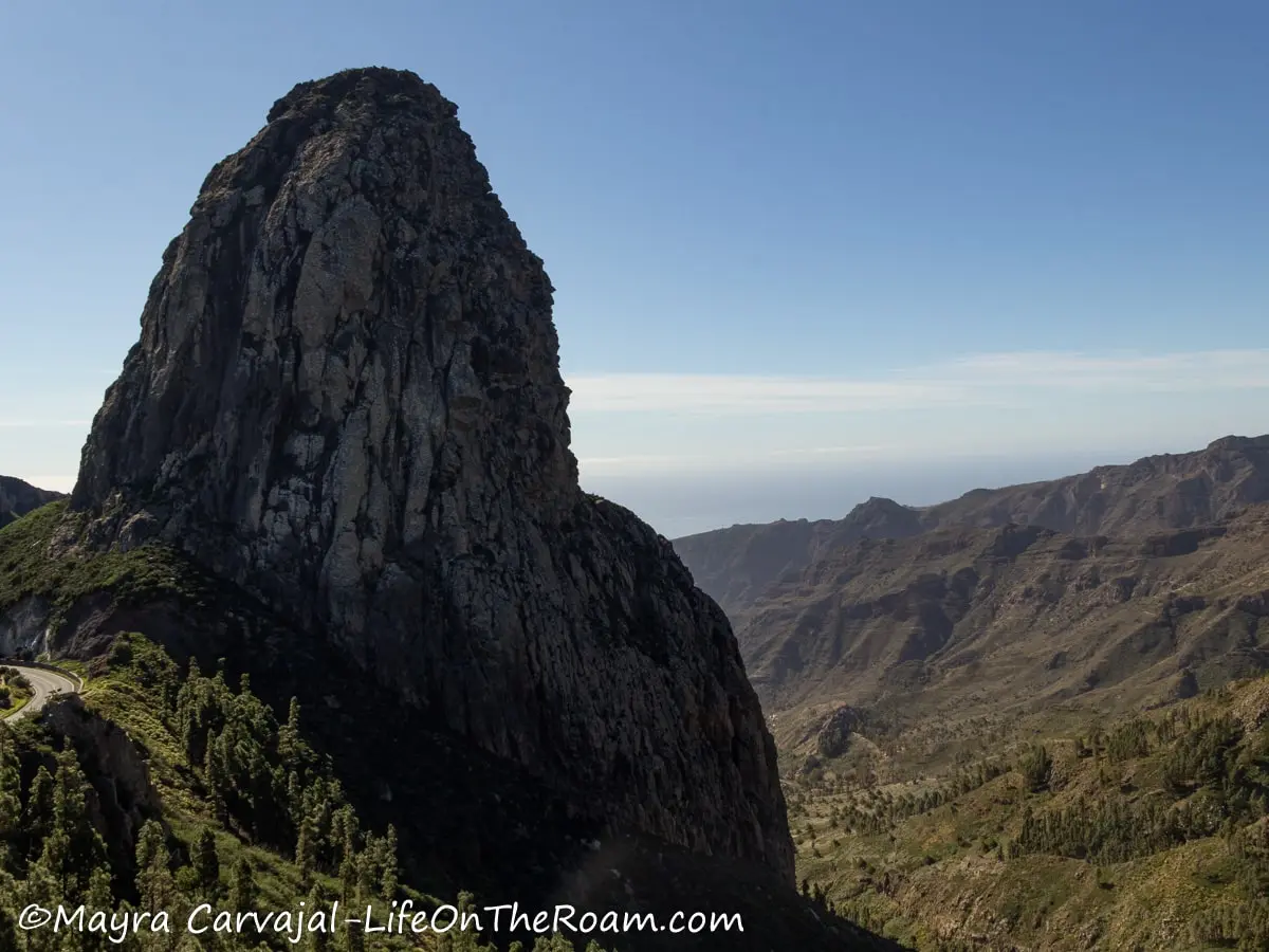 A huge rock formation partially covered in vegetation with a mountain in the distance