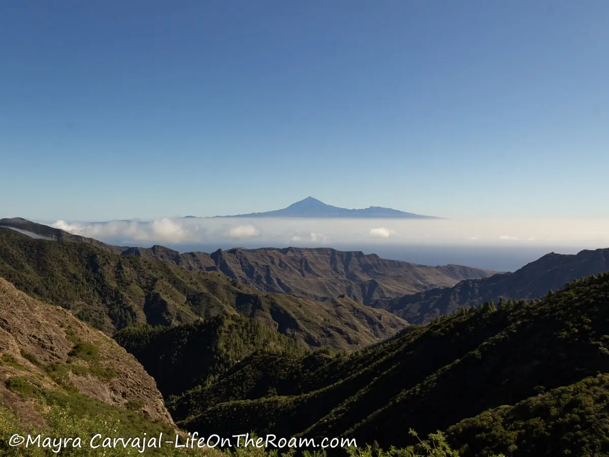 Mountain ridges covered in vegetation with the view of a volcano peak in the distance partially covered by clouds