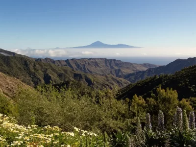 View of mountain ridges covered in green with a volcano peak in the far distance