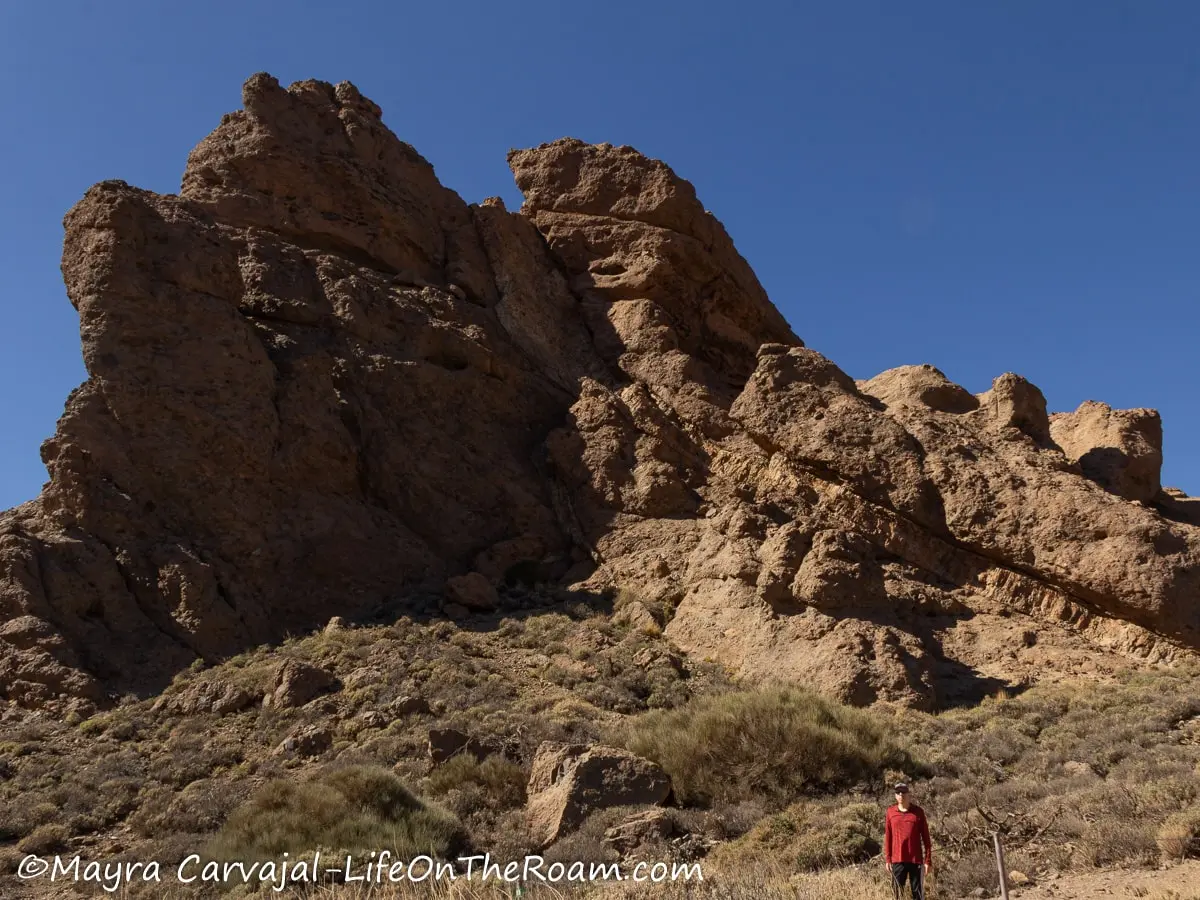 A man standing next to a big rock formation in the shape of a mountain