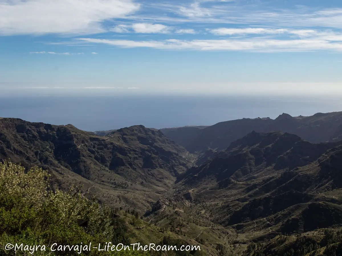 View of extensive mountain ridges and ravines converging in a valley with the sea in the background